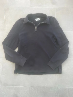 Mörkblå zip-tröja från East West - En svart långärmad tröja från East West med halvzip och krage. Tröjan har en enkel och clean design och passar till många olika sammanhang.