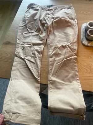Beiga chinos från Zara Man - Snygga beiga chinos från Zara Man Basic Collection. Klassisk rak passform med fickor fram och bak, tillverkade i mjukt bomullstyg. Perfekta för en clean och avslappnad stil. Stängs med knapp och dragkedja.