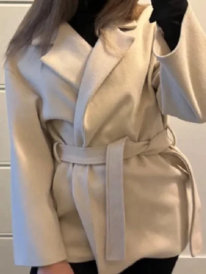 Beige kappa från MISSÄY - Stilren beige kappa med bred krage och knytskärp i midjan från Missäy. Kappan har en rak passform och är tillverkad i ett mjukt tyg som ger en lyxig känsla. Perfekt för att lyfta din outfit under kyliga dagar. 