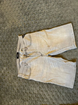 Ljusgrå jeansshorts från Replay - Säljer ett par ljusgrå jeansshorts från Replay med klassisk femficksdesign och bälteshällor. Shortsen har dragkedja och knapp framtill och är tillverkade i ett mjukt denimtyg. Perfekta för en avslappnad och stilren look.