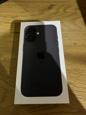 iPhone 16 svart 128GB - Snygg iPhone 16 i svart med 128GB lagring. Telefonen har en stilren design med två kameror på baksidan och Apples klassiska logga. Tillverkad i glas och aluminium, perfekt för dig som gillar modern teknik och enkel stil.