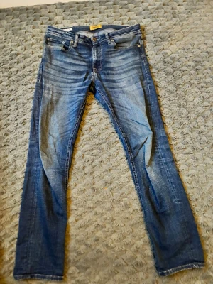 Blå slim fit jeans från Jack and jones - Snygga blå slim fit jeans från Jack and Jones med klassisk femficksdesign och slitna detaljer. Jeansen har en medelhög midja, dragkedjegylf och är tillverkade i bomullsdenim med stretch för extra komfort.