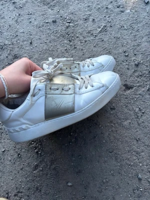 Vita sneakers med guld från Valentino - SKRIV FÖR FLER BILDER PRIS KAN DISKUTERAS. Säljer dessa snygga vita sneakers från Valentino med metallic guld över skon då dom inte passar när jag köpte dom. Skorna har vita snören och detaljerad sula. Perfekta för dig som vill ha en lyxig och trendig look.