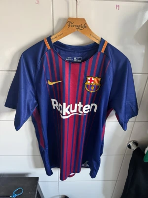 FC Barcelona matchtröja Iniesta #8 - Snygg FC Barcelona matchtröja från Nike med A. Iniesta och nummer 8 på ryggen. Tröjan är blå med röda vertikala ränder, gula detaljer och klubbmärke på bröstet. Tillverkad i lätt och ventilerande material, perfekt för fotboll eller som supporterplagg.