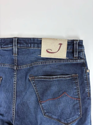 Mörkblå jeans från Jacob cohen - Snygga mörkblå jeans från Jc Brand med klassisk femficksmodell och raka ben. Jeansen har kontrastsömmar och en beige patch med ett rött Jc på bakfickan. Tillverkade i mjuk denim med en stilren look som passar till det mesta.