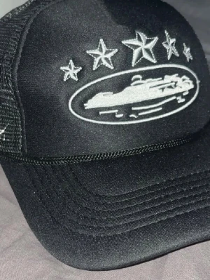 Corteiz keps - Svart keps med mesh på sidorna och broderade vita stjärnor framtill och på sidan. Framsidan har även ett broderat motiv av en bil i vitt. Snygg och sportig stil som sticker ut.  