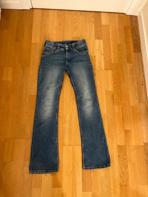 Blå bootcut jeans med slitningar - Ett par klassiska blå bootcut jeans med lätt slitna detaljer och utsvängda ben. Är lite upptrampade och har en lite fläck på knät!💕
