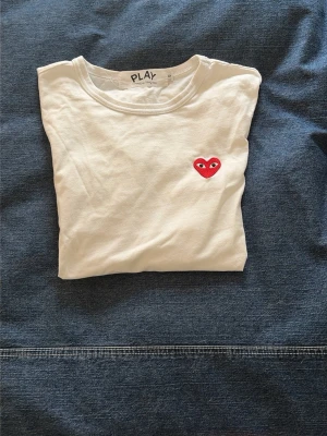 Vit Comme des Garçons PLAY t-shirt - Tjena! Säljer denna snygga vita t-shirten från Comme des Garçons PLAY i storleken S men passar även Xs. Perfekt nu till sommaren och är även i väldigt bra skick för endast 399🤩!! Skriv gärna som ni har några frågor!🙌