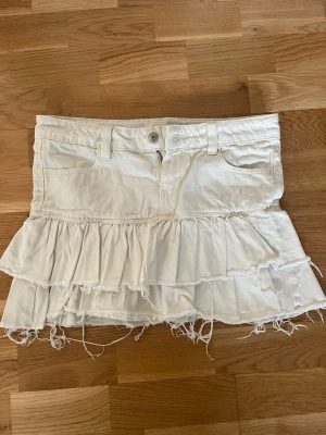 Low waist Vit volangkjol i jeans tyg - Snygg vit kortkjol med volanger och fransiga kanter. Kjolen är låg midjad!! 