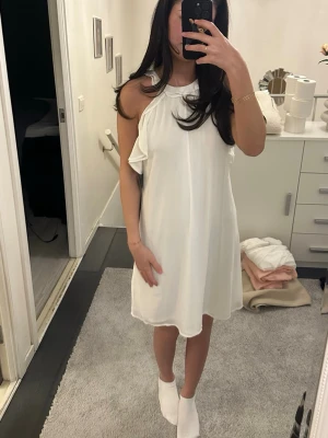 Vit klänning  - Säljer en vit oneshoulderklänning från Hey med volangdetalj längs axeln. Klänningen är kort och har en lös passform, perfekt för dig som gillar en stilren och fräsch look. Materialet känns lätt och luftigt.