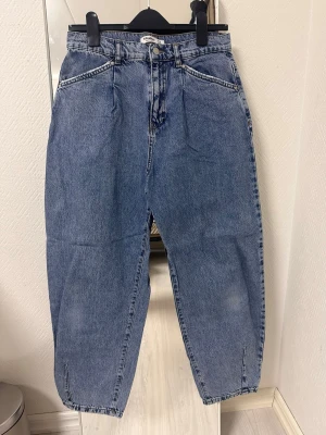 Blå baggy jeans från Pull&Bear - Baggy jeans i klassisk blå denim från Pull&Bear. Hög midja, avslappnad passform och raka ben med lätt avsmalnande avslut. Femficksmodell med dragkedja och knapp. Perfekta för en chill och trendig look.