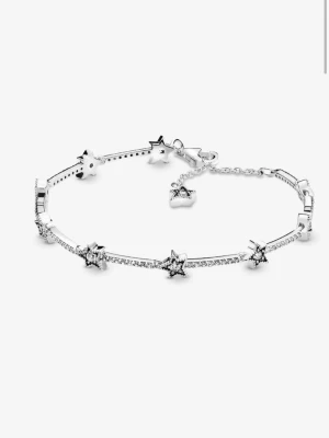 Silverarmband med stjärnor från Pandora - Ett elegant silverarmband från Pandora med gnistrande stjärnformade detaljer och små kristaller. Armbandet har en tunn kedja och justerbar låsning, perfekt för att ge en glittrande touch till din stil. Stjärnorna är utsmyckade med små stenar för extra effekt. Nypris 1199kr