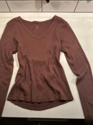 Brun v-ringad topp från Brandy Melville - Säljer en brun långärmad topp från Brandy Melville i ribbad bomull. Toppen har v-ringning och en slim passform. Det står ingen storlek på tröjan men jag skulle säga att den passar xs-s 