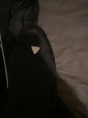 Svart pufferjacka från Guess - Snygg svart pufferjacka från Guess med huva och dragkedja framtill. Jackan har en quiltad design och en tydlig logotyp på axel. Perfekt för kalla dagar och har en modern, sportig look. Dragkedja finns inte detta är den enda problemet men annars är den perfekt 