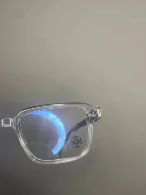 Chrome Heart glasögon  - Snygga glasögon med transparent fyrkantig båge och svarta mönstrade detaljer på skalmarna. Ramen är i plast och ger en modern och stilren look. Perfekt accessoar för att lyfta din outfit.