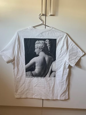 Vit t-shirt med statyprint och text - Vit t-shirt med svartvit print av en klassisk staty på ryggen och text.
