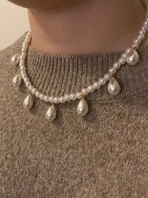 Pärlhalsband med droppformade hängen - Snyggt halsband med vita runda pärlor och droppformade pärlhängen. Halsbandet har guldfärgade detaljer mellan pärlorna och ger en elegant och trendig look. Perfekt accessoar för att lyfta din outfit med en klassisk touch.