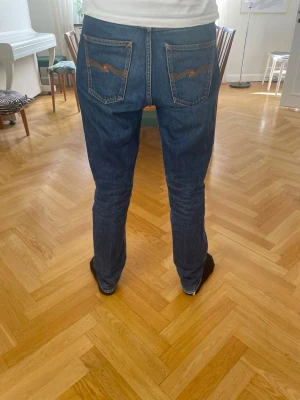 Mörkblå Nudie Jeans Gritty Jackson - Säljer ett par mörkblå slim fit jeans från Nudie Jeans med klassiska bakfickor och orangea sömmar. Jeansen har fem fickor och är tillverkade i denim med snygg tvätt och detaljer. Perfekt för dig som gillar en stilren och modern look.