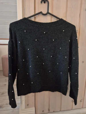 Svart stickad tröja med pärlor H&M - Mysig svart stickad tröja från H&M med dekorativa vita pärlor över hela tröjan. Långärmad modell med rund halsringning och mjukt material som passar perfekt till jeans eller kjol.