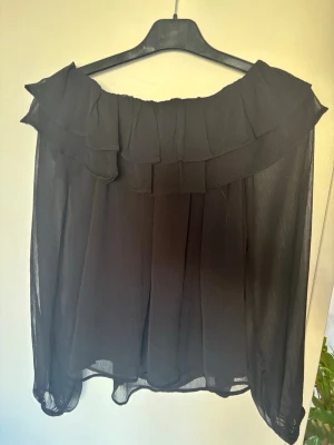 Svart offshoulder blus med volang - Snygg svart offshoulder blus. Blusen har ett luftigt fall och långa ärmar i samma lätta material!