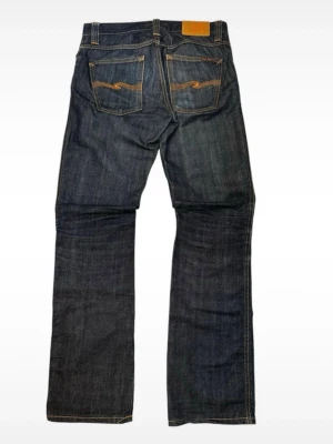Mörkblå jeans från Nudie Jeans - Snygga mörkblå jeans från Nudie Jeans med klassisk rak passform. Storlek W=30 och L=32.Jeansen sitter riktigt bra och är nästan helt oanvända. Skriv om du har några frågor. Totallängd=103cm, Midja=40cm, benöppning=20cm
