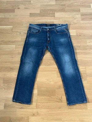 Blå raka jeans från Replay - Säljer ett par klassiska blå jeans från Replay med raka ben och fem fickor. Jeansen har snygga slitningar och kontrastsömmar samt en patch med Replay-logga bak i midjan. Perfekta till en avslappnad stil och tillverkade i bomull.