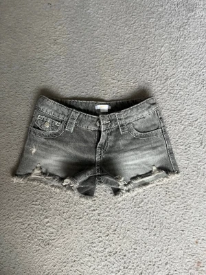 Grå jeansshorts med slitningar - Snygga grå jeansshorts med slitna detaljer och fransig kant. Klassisk femficksmodell med broderade bakfickor och knappstängning. Perfekta för en avslappnad och trendig look.