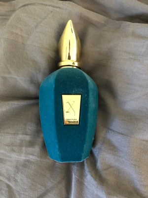 Xerjoff Erba Pura parfym blå/guld - Lyxig parfymflaska från Xerjoff, modellen Erba Pura. Flaskan är klädd i sammetsliknande blått material och har en elegant guldfärgad kork. Framsidan pryds av en guldfärgad etikett med logga och namn. Perfekt för dig som gillar exklusiva dofter och snygg design.