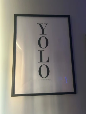 YOLO poster  - Stilren poster med texten YOLO (You Only Live Once) i stora svarta bokstäver på vit bakgrund. Postern är inramad i en tunn svart ram och passar perfekt som väggdekoration för att ge rummet en modern och personlig touch. RAM INGÅR EJ‼️