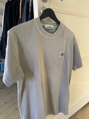 Grågrön t-shirt från Stone Island - Snygg grå t-shirt från Stone Island med klassisk logotyp-patch på bröstet. T-shirten har rund halsringning och korta ärmar. Tillverkad i mjuk bomull för en skön känsla och stilren look.