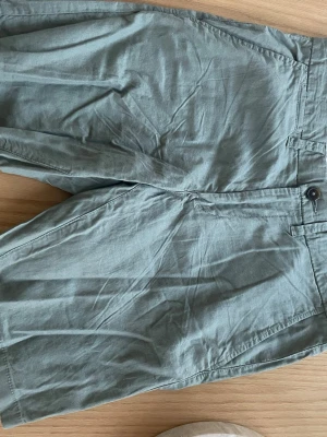 Gröna linne shorts  - Snygga gröna shorts i linne med klassisk passform. Shortsen har sidofickor, bakfickor med knapp och stängs med knapp och dragkedja framtill. Perfekta för varma dagar och enkel att matcha med olika toppar.
