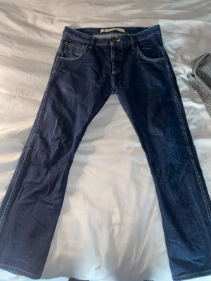 Mörkblå jeans från Wrangler W32xL34 - Snygga mörkblå jeans från Wrangler med klassisk femficksdesign och raka ben. Jeansen har kontrastsömmar och tydliga W-detaljer på bakfickorna. Perfekta för en avslappnad och stilren look.