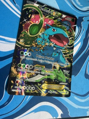 Venusaur EX Pokémonkort XY123 - Säljer ett Venusaur EX Pokémonkort med nummer XY123. Kortet har en färgstark och glansig design med Venusaur i fokus och detaljer i grönt, blått och guld. Perfekt för samlare eller Pokémonfans som vill utöka sin kortsamling.