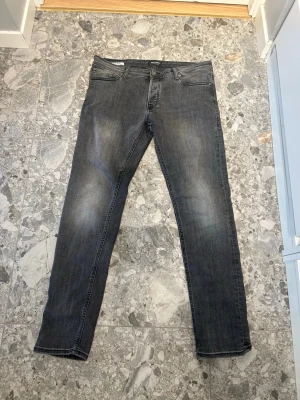 Grå jeans - Snygga grå slim fit jeans med klassisk femficksdesign och lätt slitning på låren. Jeansen har normal midja och raka ben, perfekta för en avslappnad och trendig look. Passar till det mesta och är ett måste i garderoben.