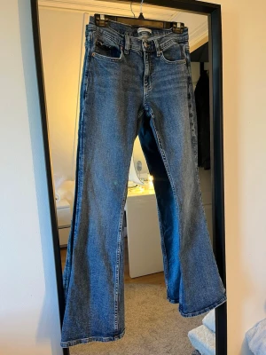 Blå bootcut jeans, midwaist - Säljer ett par klassiska blå bootcut jeans med fem fickor. Jeansen har en snygg tvättad look och vida ben. Använda ett par fåtal gånger, ej slitna