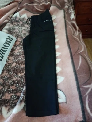 Svarta halv långa byxor från Vogue stl XL - Svarta mjukisbyxor från Vogue med resår och dragsko i midjan. Byxorna har raka ben och är tillverkade i ett mjukt och bekvämt material. Perfekta för en avslappnad stil och passar till många olika tillfällen. Nylon och viskos. Oanvända helt nya o ligger i sin originalförpackning.