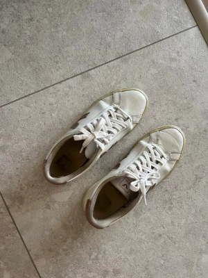 Vita Veja sneakers med rosa detaljer  - Säljer dessa vita veja sneakers med rosa detaljer i storlek 40. Har använts mycket därav hål i hälen på insidan av skon men inget som syns!