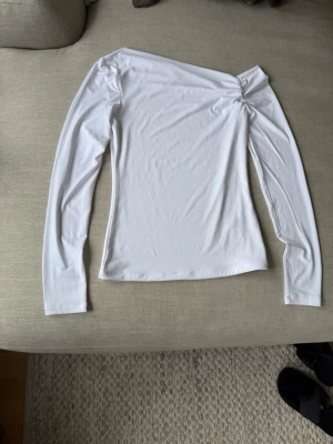Vit oneshoulder topp från BikBok - Snygg vit långärmad topp från BikBok med oneshoulder-design och lätt rynkdetalj vid axeln. Toppens material känns mjukt och stretchigt, perfekt för en trendig look. Passar dig som gillar stilrena och moderna plagg.