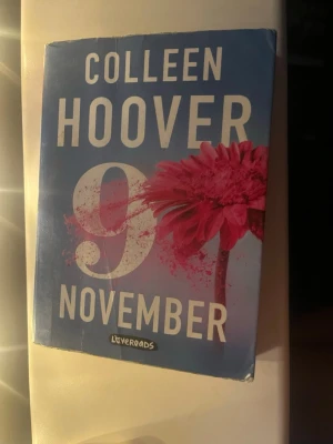 9 November av Colleen Hoover - En gripande kärleksroman av Colleen Hoover med blått omslag och stor rosa blomma. Boken handlar om Fallon och Ben som möts samma dag varje år. Perfekt för dig som gillar romantik och starka känslor. Mjukt omslag i papper.