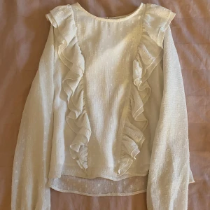 Vit blus med volang från Gina tricot - Säljer en vit blus från Gina tricot med volangdetaljer framtill och vid ärmen längst ner. Superfin till våren när man vill klä upp sig lite.