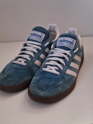 Adidas Handball Spezial  - Snygga Adidas Handball Spezial sneakers i blå mocka med vita detaljer och dom klassiska tre Adidas ränderna på sidorna. Skorna har vit plös med blå logga och bruna gummisulor. 