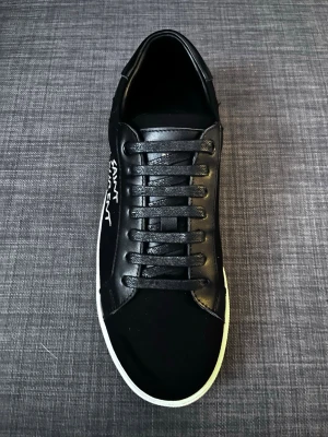 Svarta Saint Laurent sneakers och allt ingår som exempel skobox skopåse och kort - Svarta sneakers från Saint Laurent med vit sula och klassisk låg profil. Skon har svarta skosnören, läderdetaljer och Saint Laurent-logga i vitt på sidan samt guldtext på innersulan. Snygg och stilren design som passar till många outfits.