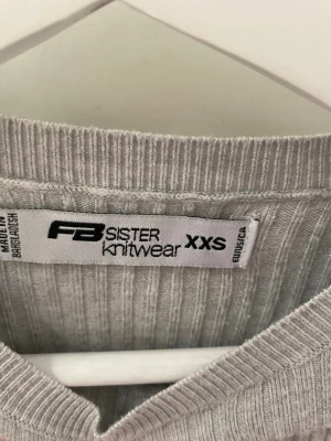 Grå ribbad tajt topp från new yorker med detaljer  - Säljer en ljusgrå ribbad topp från new yorker i storlek XXS. Toppen har en tight passform, rund halsringning och dekorativ kant längst ner och vid händerna . Materialet är mjukt och stretchigt, perfekt för en enkel och clean look. Aldrig använt 