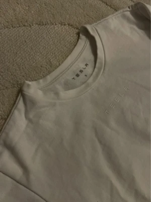 Vit sweatshirt från Tesla - Vit sweatshirt från Tesla med diskret broderad logga på bröstet. Tröjan har rund halsringning och långa ärmar. Tillverkad i mjukt material som känns skönt mot huden. Perfekt för en clean och stilren look.