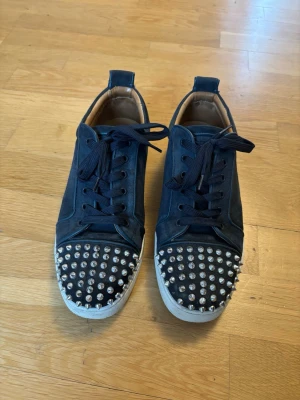Marinblå louboutins med nitar - Säljer mina navy blue louboutin sneakers med silvriga piggar. Storleken är 42,5 men passar superbra om man har 42. Undersidan är inte rengjord då jag ej hunnit, men borde gå rätt smidigt o göra själv. En nit är borta, dock följer det med 3st extra nitar som man själv kan sätta fast. Extra skosnören medföljer, samt original dustbags. Skriv gärna vid övriga frågor!