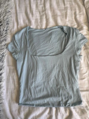 Ljusblå topp med fyrkantig ringning - Trendig ljusblå topp med korta ärmar och fyrkantig ringning. Tunn och mjuk i materialet, perfekt för en stilren och enkel look. Passar bra till både jeans och kjol.