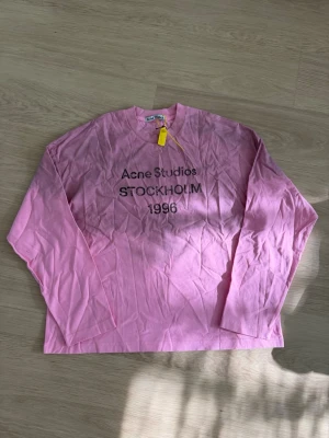 Rosa långärmad t-shirt Acne Studios - Snygg rosa långärmad t-shirt från Acne Studios med tryck 'STOCKHOLM 1996' på bröstet. Tillverkad i mjuk bomull och har en avslappnad passform. Perfekt för en trendig och avslappnad stil.