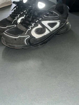 Dior B30 - Svarta sneakers från Diod med coola vita och reflekterande detaljer längs sidorna och ovandelen. Skorna har en chunky sula och ovandel i mesh och syntetmaterial för en sportig vibe. Perfekta för dig som gillar streetwear och vill sticka ut. Box och allt ingår!