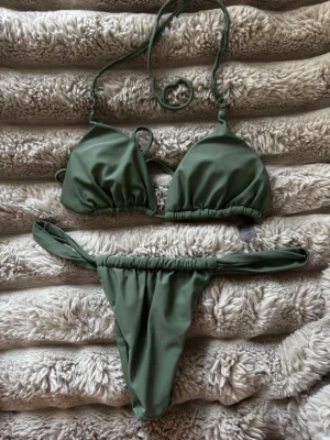 Grön bikini med knyt från mexiko  - Snygg grön bikini med trekantsöverdel och knyt i nacken samt ryggen. Underdelen har smala band i sidorna och enkel, stilren design. Perfekt för stranden eller poolen. Tillverkad i mjukt syntetmaterial som torkar snabbt.