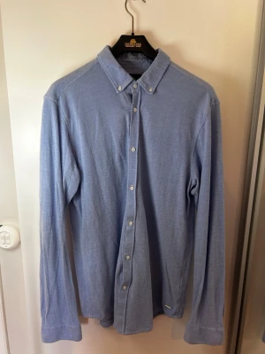Ljusblå skjorta från Scotch & Soda - Snygg ljusblå skjorta från Scotch & Soda med klassisk krage och knappar hela vägen. Skjortan har lång ärm och är tillverkad i ett mjukt bomullstyg. Perfekt för en stilren look.